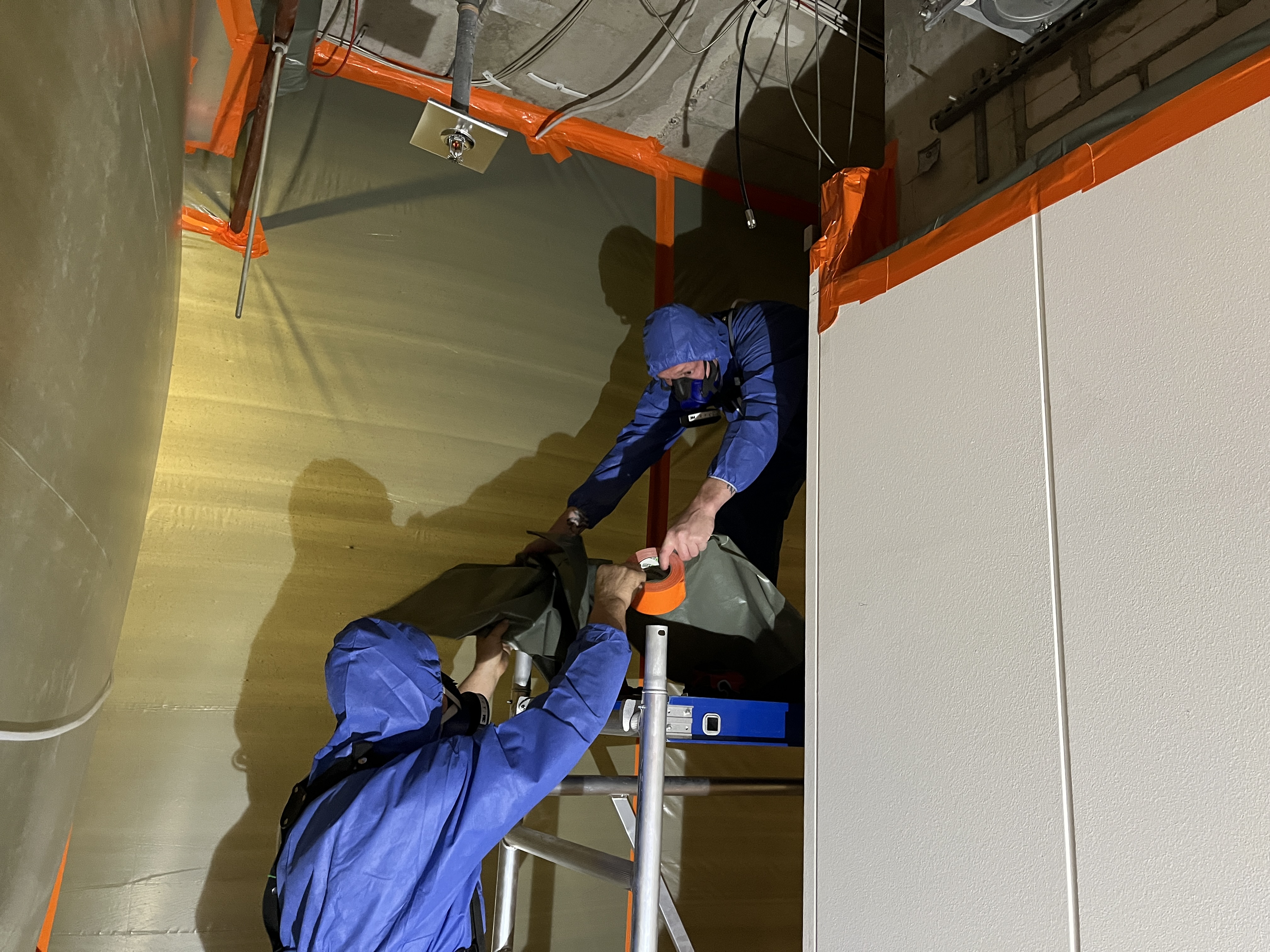 Fachkr&auml;fte in Schutzkleidung beim Ausbau belasteter Bauteile in einem abgeschotteten Bereich